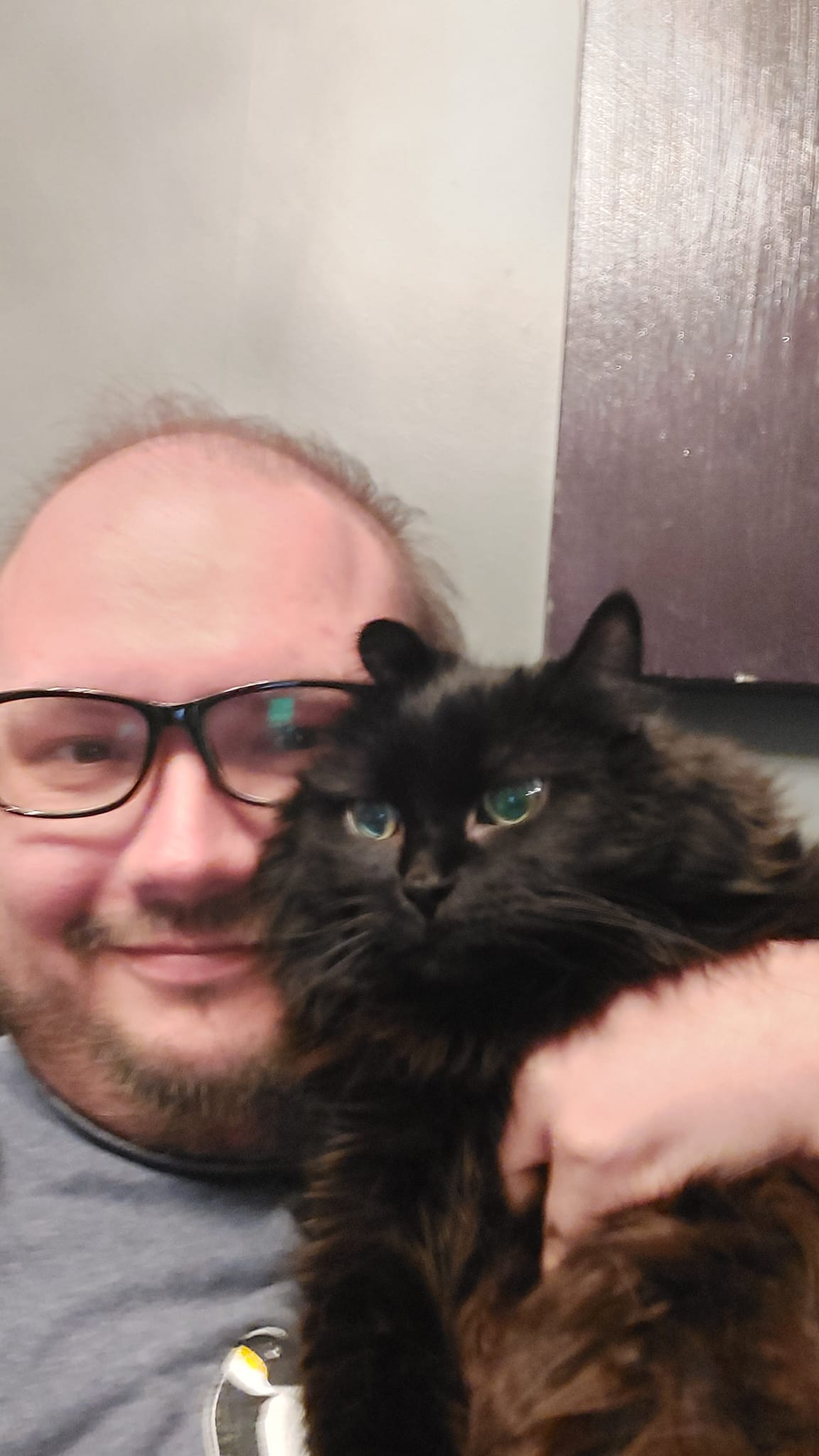 A man sits holding a fluffy black cat, she appears to be a little annoyed